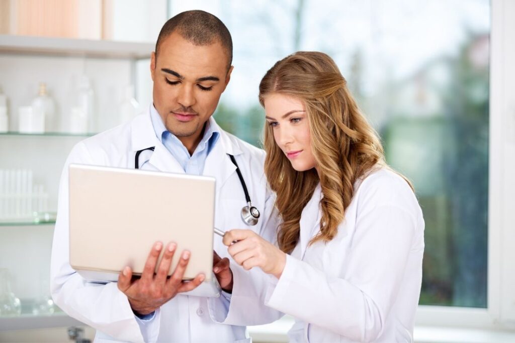 Two healthcare professionals, a man and a woman, reviewing information on a laptop in a clinical setting, symbolizing teamwork in provider onboarding.