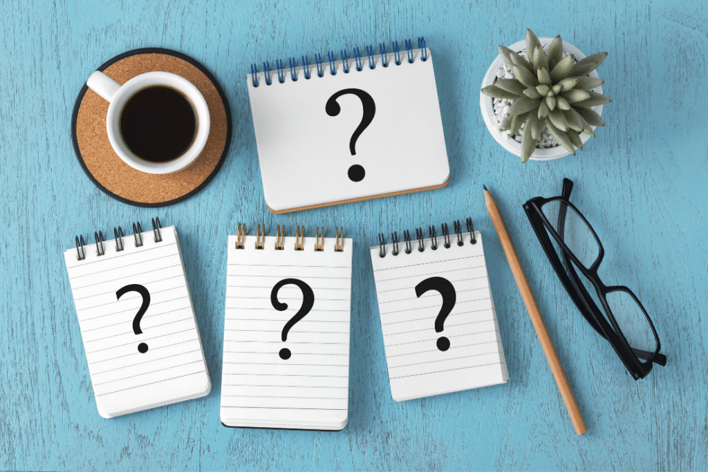 A workspace with coffee, notepads featuring question marks, and a plant, symbolizing curiosity and the exploration of why becoming MD-Staff certified is beneficial.