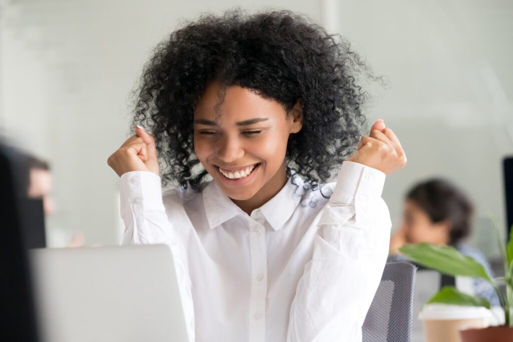Young woman smiling and celebrating in front of her laptop, expressing excitement and happiness