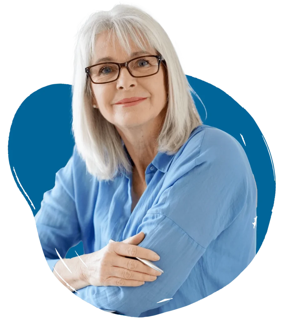 A mature woman with gray hair and glasses, wearing a blue shirt and smiling warmly. She has her arms crossed, and a blue abstract background is behind her.