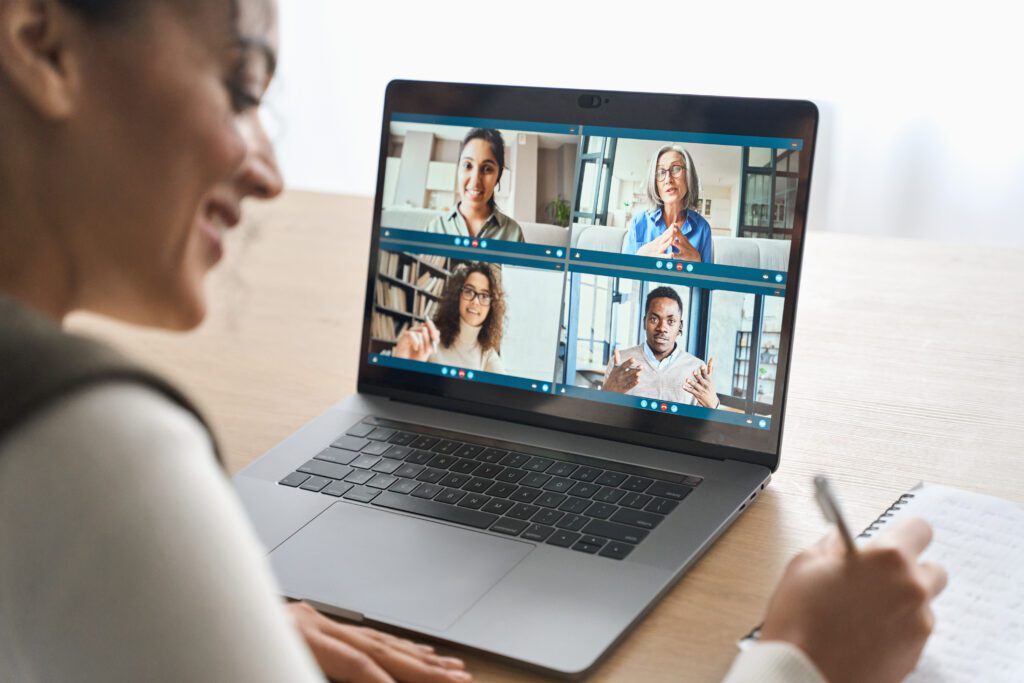 Person attending a webinar on a laptop with four speakers visible on the screen while taking notes.