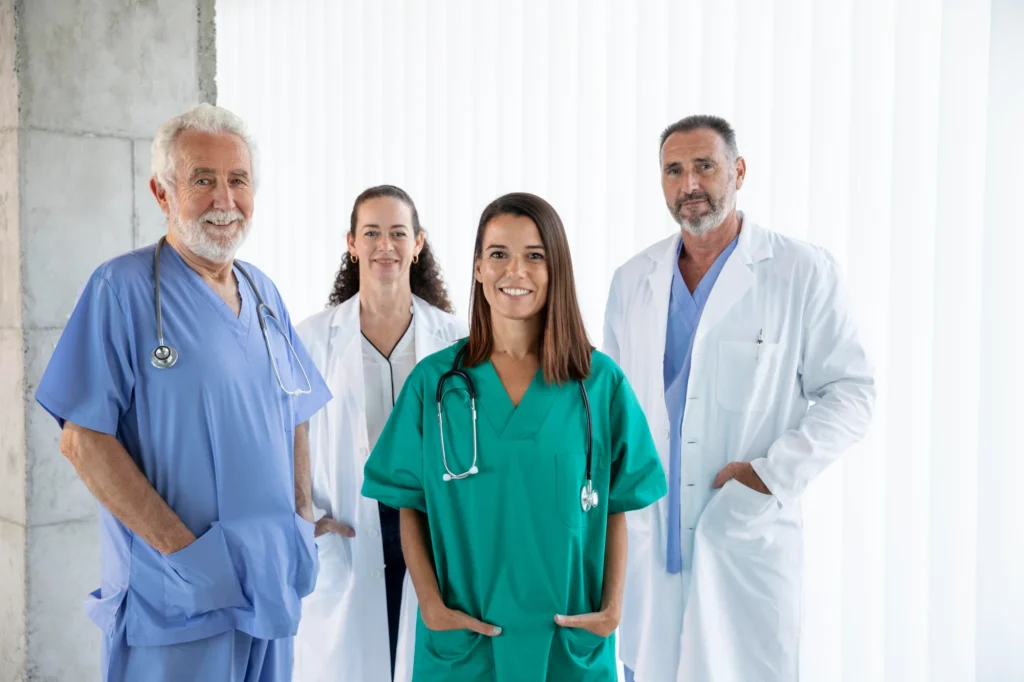 A diverse group of medical professionals standing together, smiling, and dressed in their medical attire, including scrubs and lab coats.