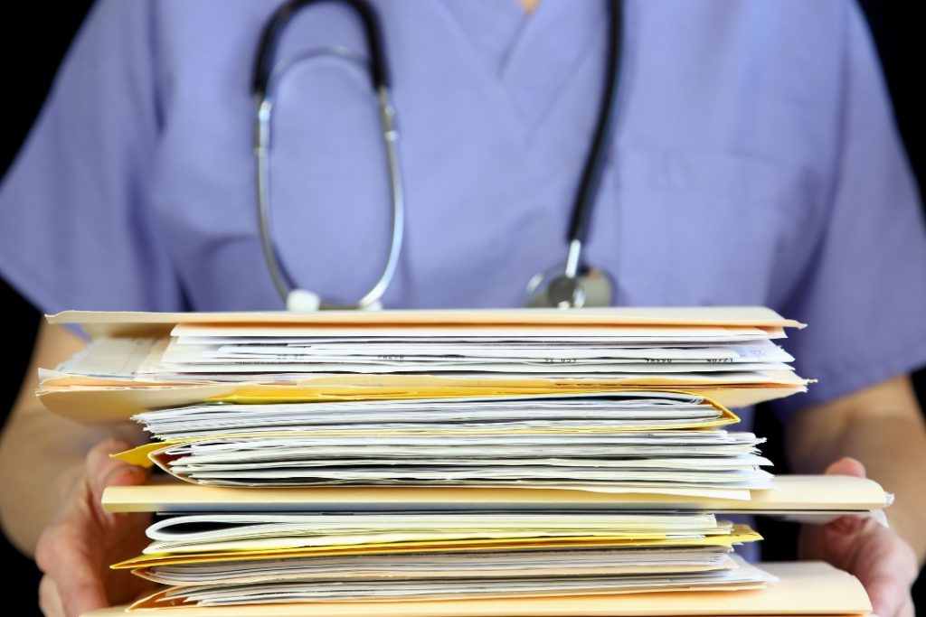 Healthcare professional holding a large stack of paper files representing manual credentialing processes.