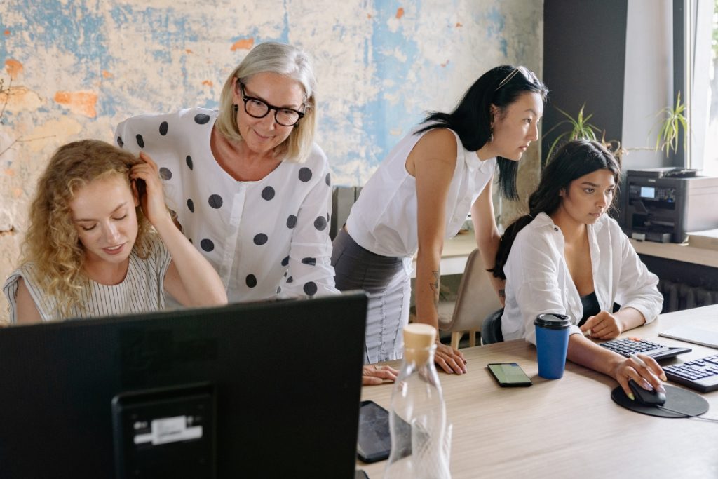 Photo of four ladies surrounding computers in an office.
