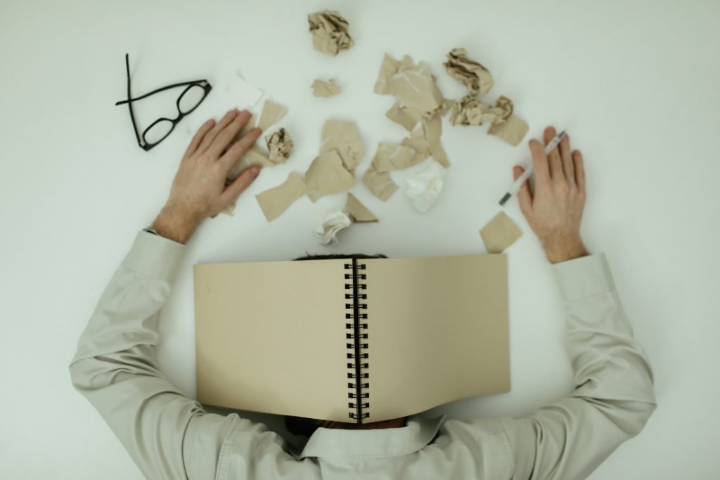 Photo of a person laying under a notebook with scattered paper everywhere.